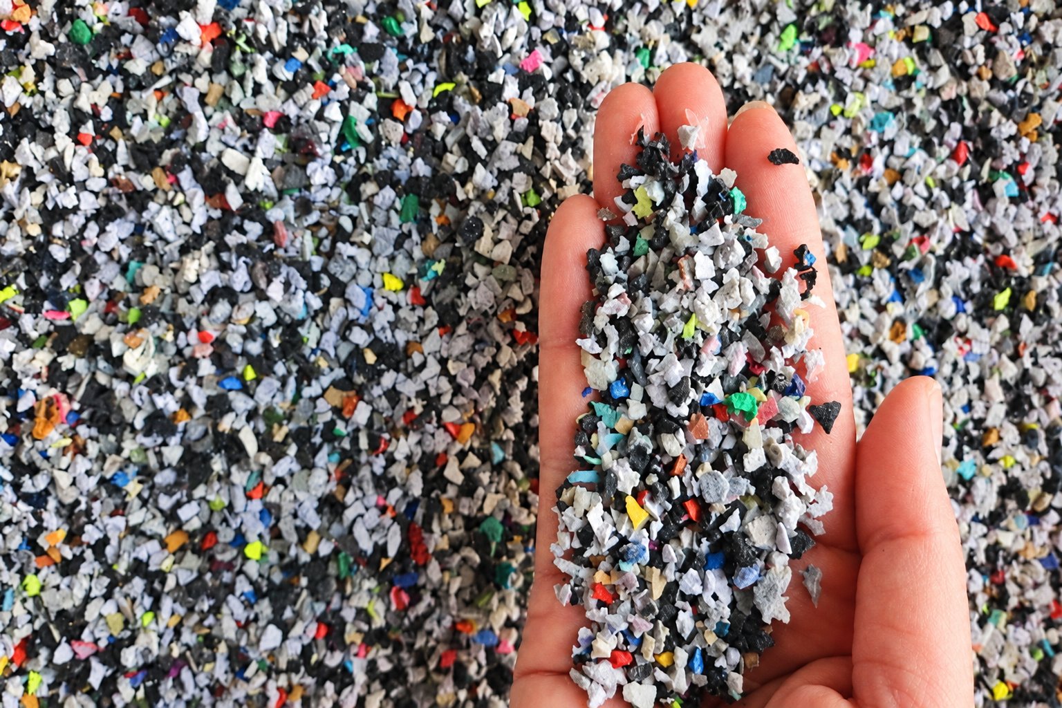 A hand holding multicoloured recycled shoe-rubber granules.