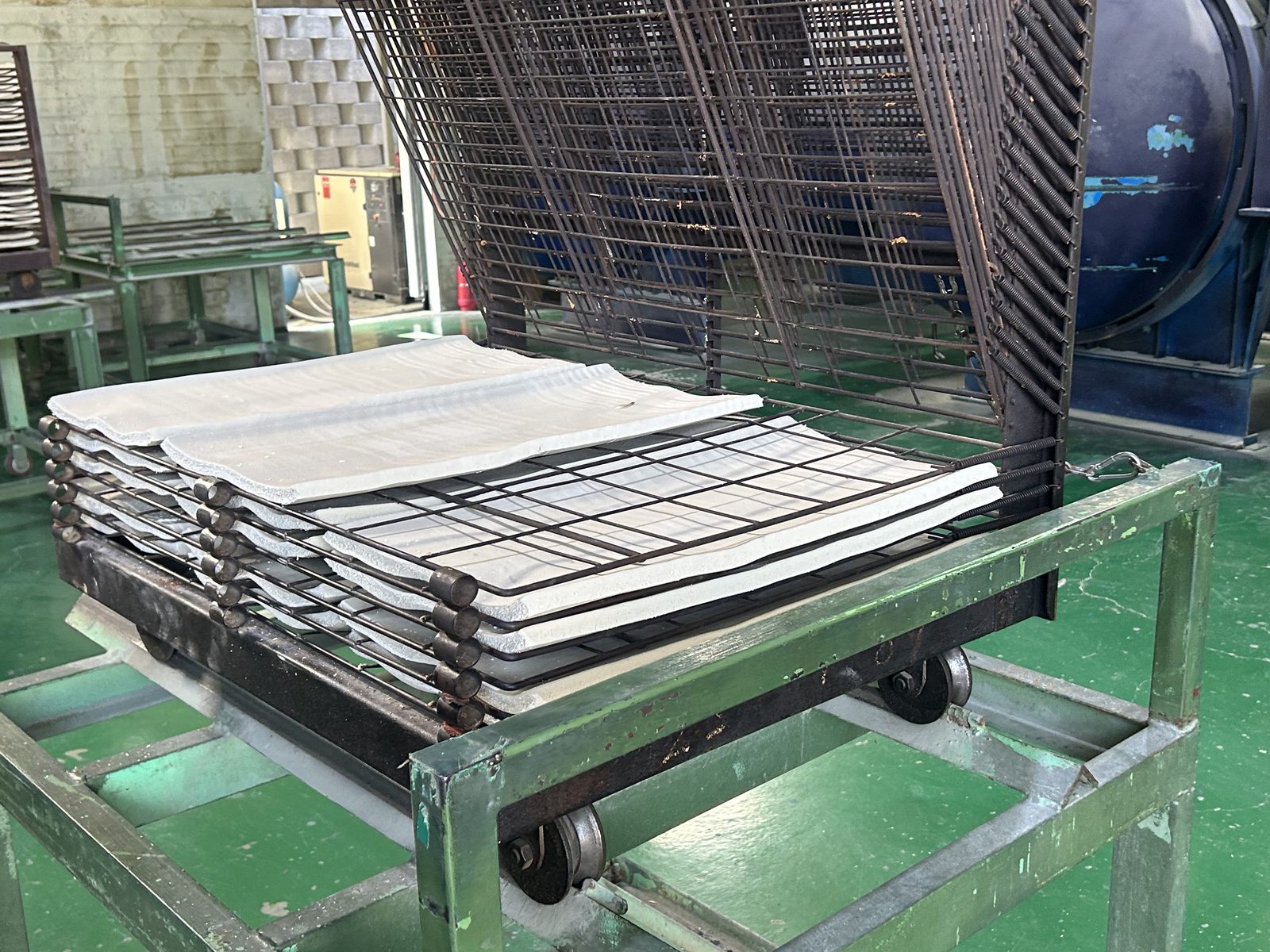 Moulded rubber sheets stacked on a rack beside a curing vessel.