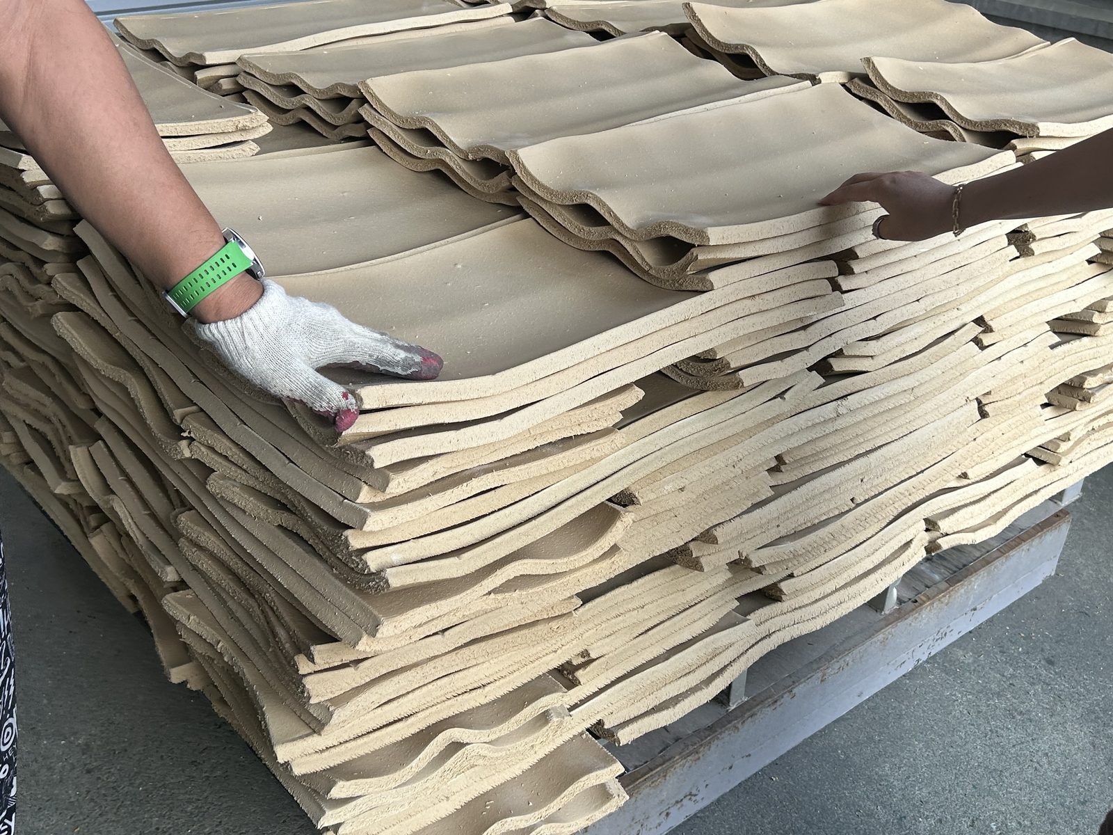 A gloved hand lifting a cured rubber sheet from a stack.