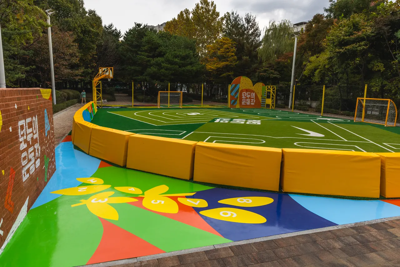 A play surface with flower graphics beside the sports field and its padded edge.